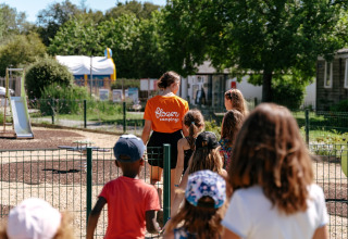 Kinderen volgen een begeleider in oranje Flower Campings-shirt op een speelplein in Bretagne, Frankrijk.