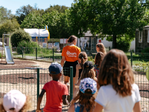 Bambini seguono un adulto con maglietta arancione Flower Campings in un parco giochi della Bretagna, Francia.