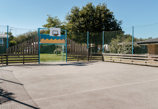 En udendørs basketballbane på Flower Camping Le Kerarno i Bretagne, Frankrig, under en klar blå himmel.