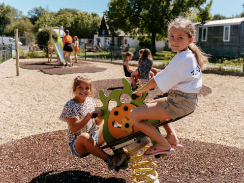 Zwei Mädchen spielen auf einer Wippe auf dem Spielplatz von Flower Camping Le Kerarno in der Bretagne, Frankreich.