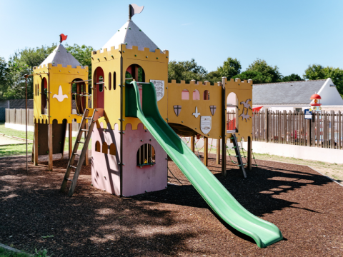 Parque infantil estilo castillo con tobogán verde en Flower Camping Le Kerarno, parque vacacional en Bretaña.