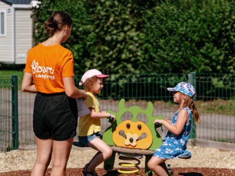 Bambini giocano nel parco giochi sorvegliati da un adulto al Flower Camping Le Kerarno, Bretagna, Francia.