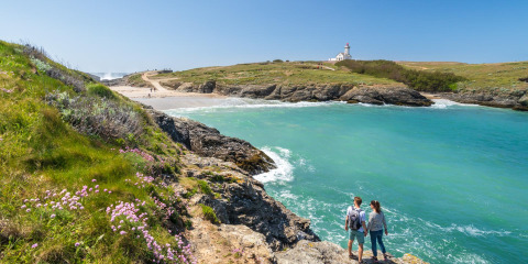 Paar steht auf Felsen mit Blick auf eine türkisfarbene Bucht, Strand und Leuchtturm in der Bretagne, Frankreich.