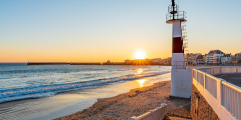 Solnedgang ved stranden i nærheden af Saint-Philibert, Bretagne, Frankrig, med fyrtårn og landsby i baggrunden.