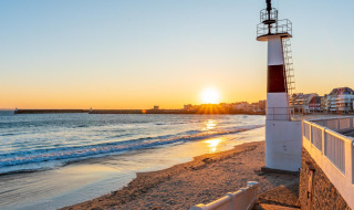 Tramonto sulla spiaggia vicino a Saint-Philibert, Bretagna, Francia, con faro e case del villaggio sullo sfondo.