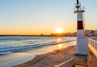 Tramonto sulla spiaggia vicino a Saint-Philibert, Bretagna, Francia, con faro e case del villaggio sullo sfondo.