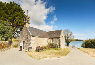 Piccola cappella di pietra a Saint-Philibert, Bretagna, Francia, con ciclisti e fiori vicino a un lago.