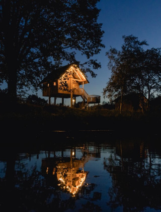 Nachtelijk beeld van een gezellig verlicht huisje op palen aan het water bij Holiday Park Mölke in Overijssel.