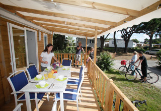 Une famille prend un repas sur la terrasse d’un mobil-home tandis que d’autres font du vélo au camping.