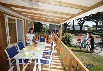 Una familia prepara la mesa en la terraza de una casa móvil mientras otros pasean en bicicleta por el camping.