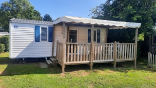 Mobile home Stacaravan Confort 28m2 with wooden porch, canopy, and blue shutters, on grassy lawn.