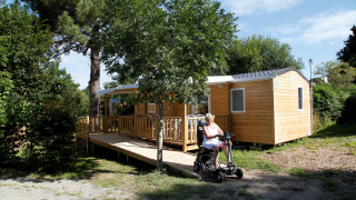 Mujer en scooter eléctrico frente a la casa móvil Comfort Stacaravan PMR 29m2 con rampa en entorno natural.