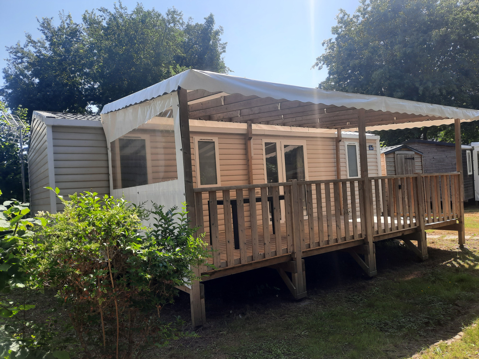 Buitenaanzicht van Comfort stacaravan 32m2 met overdekt houten terras en omheining in het zonlicht.