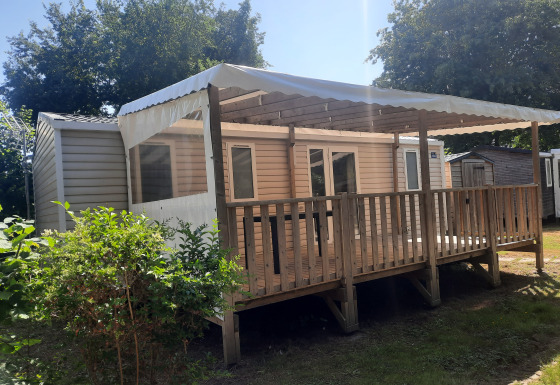 Außenansicht des Comfort Stacaravan 32m2 mit überdachter Terrasse und Holzzaun im Sonnenschein.