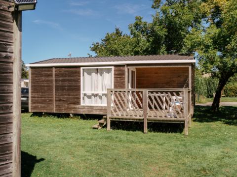 Mobil-home Comfort Stacaravan 22m2 avec terrasse en bois sur pelouse verte, entouré d’arbres.
