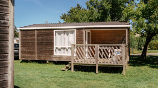 Komfortable Mobilheim Comfort Stacaravan 22m2 mit Holzterrasse, umgeben von grünem Rasen und Bäumen.