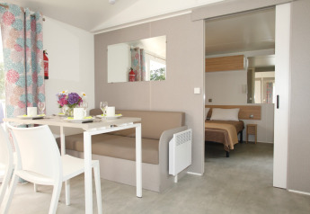 Interno della Comfort Stacaravan PMR 29m2 con tavolo da pranzo e camera da letto al Flower Camping Le Kerarno.