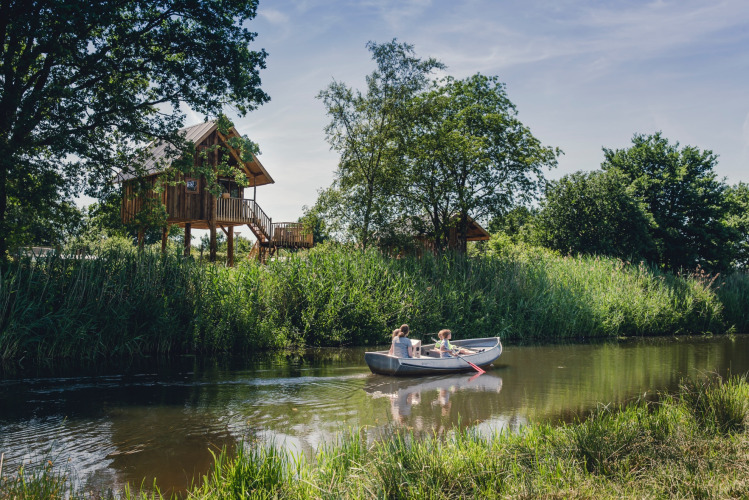 Gezin kanoot op rivier naast boomhut bij Holiday Park Mölke, Overijssel, Nederland op zomerse dag.