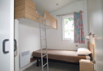 Modernes Mobilheimzimmer mit Etagenbett, Einzelbett, Fenster und buntem Vorhang im Camping Le Kerarno.