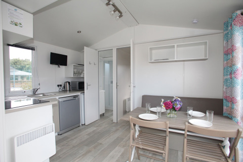 Bright modern mobile home kitchen and dining area with four plates set and a vase of flowers on table.