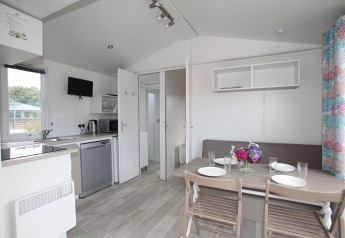 Cuisine moderne de mobil-home avec coin repas, table dressée pour quatre et bouquet de fleurs coloré.