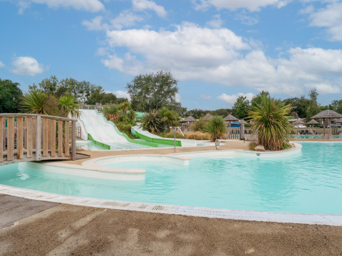 Outdoor swimming pool with waterslides, palm trees and sun loungers at Flower Camping Le Vorlen, Brittany, France.