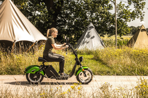 Donna su monopattino verde davanti a tende nel parco vacanze Mölke, immerso nel verde a Overijssel.