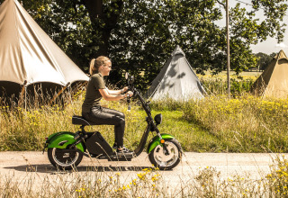 Mujer en patinete eléctrico verde pasa junto a tiendas de campaña en Holiday Park Mölke, Overijssel.