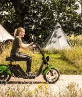 Mujer en patinete eléctrico verde pasa junto a tiendas de campaña en Holiday Park Mölke, Overijssel.