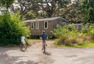 Due bambini vanno in bicicletta verso una casetta di legno a Flower Camping Le Vorlen, in Bretagna, Francia.