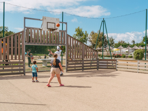 Børn og voksne spiller basketball på en udendørs bane i Flower Camping Le Vorlen, Bretagne, Frankrig.