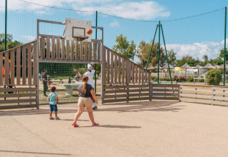 Kinderen en volwassenen spelen basketbal op een speelplein in Flower Camping Le Vorlen, Bretagne, Frankrijk.