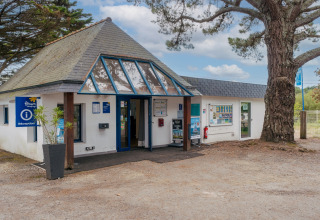 Receptiegebouw van Flower Camping Le Vorlen in Bretagne, Frankrijk met bomen en informatiepanelen.