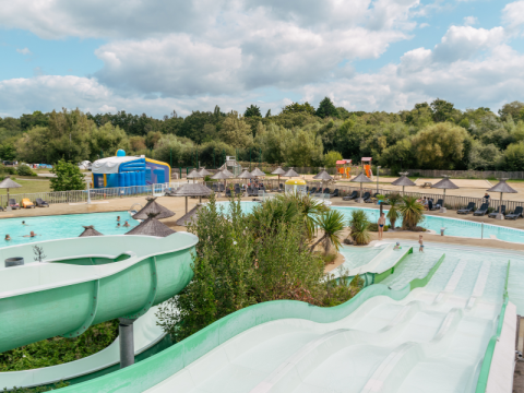 Wasserpark mit Rutschen, Pools, Liegestühlen und Sonnenschirmen in einer grünen Umgebung in der Bretagne, Frankreich.