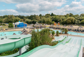 Buitenwaterpark met glijbanen, zwembaden, ligzetels en parasols in een groene omgeving in Bretagne, Frankrijk.