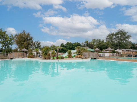 Buitenzwembad met glijbanen, palmbomen en hutjes op Flower Camping Le Vorlen in Bretagne, Frankrijk.