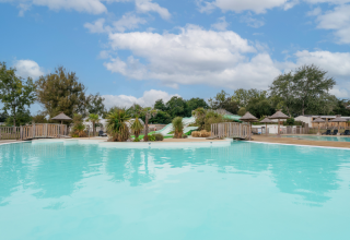 Buitenzwembad met glijbanen, palmbomen en hutjes op Flower Camping Le Vorlen in Bretagne, Frankrijk.