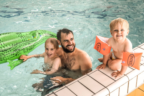 Ein Mann und zwei Kinder genießen das Schwimmen mit einer grünen Luftmatratze im Holiday Park Mölke.