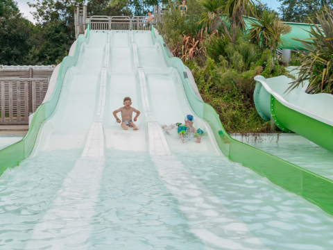 Children enjoy riding a wide water slide surrounded by plants at Flower Camping Le Vorlen in Brittany, France.