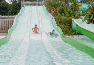 Children enjoy riding a wide water slide surrounded by plants at Flower Camping Le Vorlen in Brittany, France.