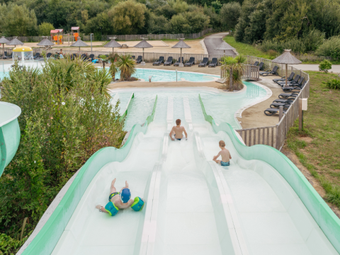 Kinderen glijden van de waterglijbaan in het zwembad van Flower Camping Le Vorlen in Bretagne, Frankrijk.