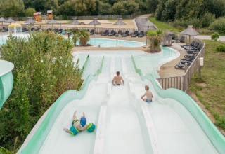 Kinder rutschen eine Wasserrutsche hinunter in einem Freizeitpark-Pool bei Flower Camping Le Vorlen in der Bretagne.