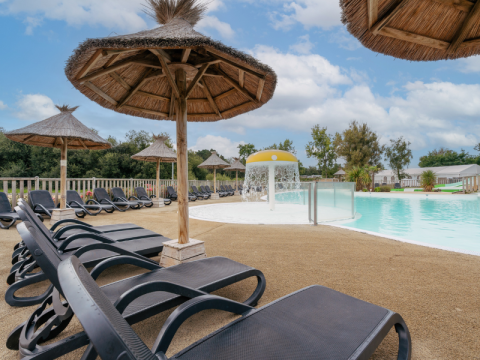 Relaxing pool area with sun loungers and thatched umbrellas at Flower Camping Le Vorlen in Brittany, France.