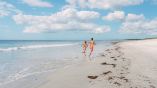 Twee mensen lopen langs het strand bij Flower Camping Le Vorlen in Bretagne onder een blauwe lucht.