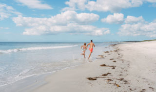 Twee mensen lopen langs het strand bij Flower Camping Le Vorlen in Bretagne onder een blauwe lucht.