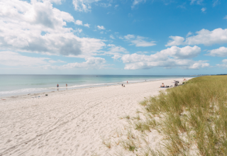 Zandstrand met duinen en enkele mensen aan zee bij Fouesnant, Bretagne, onder een blauwe lucht met wolken.