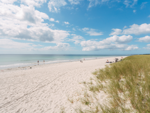 Sandstrand med klitter og spredte mennesker ved havet nær Fouesnant, Bretagne, under blå himmel med skyer.