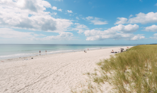 Zandstrand met duinen en enkele mensen aan zee bij Fouesnant, Bretagne, onder een blauwe lucht met wolken.