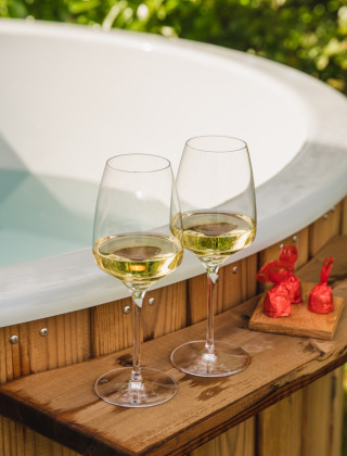 Twee glazen witte wijn, chocolaatjes en een waxinelichtje bij een houten hottub in Holiday Park Mölke, Overijssel.