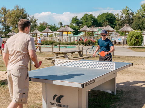 Deux hommes jouent au tennis de table en extérieur par une journée ensoleillée au Flower Camping Le Vorlen, Bretagne.
